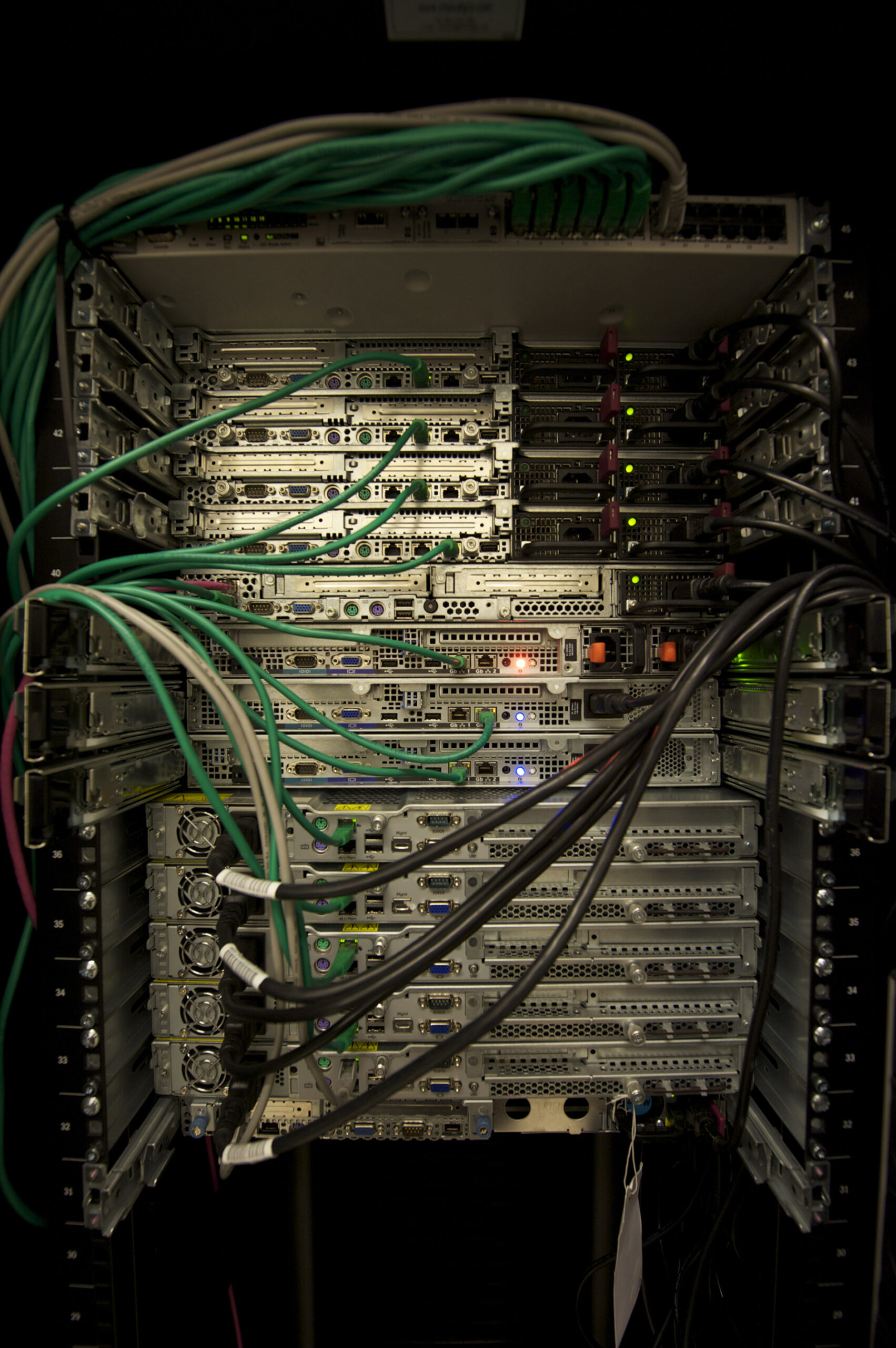 Rear view of rack-mounted servers connected by green network cables and black power cables.